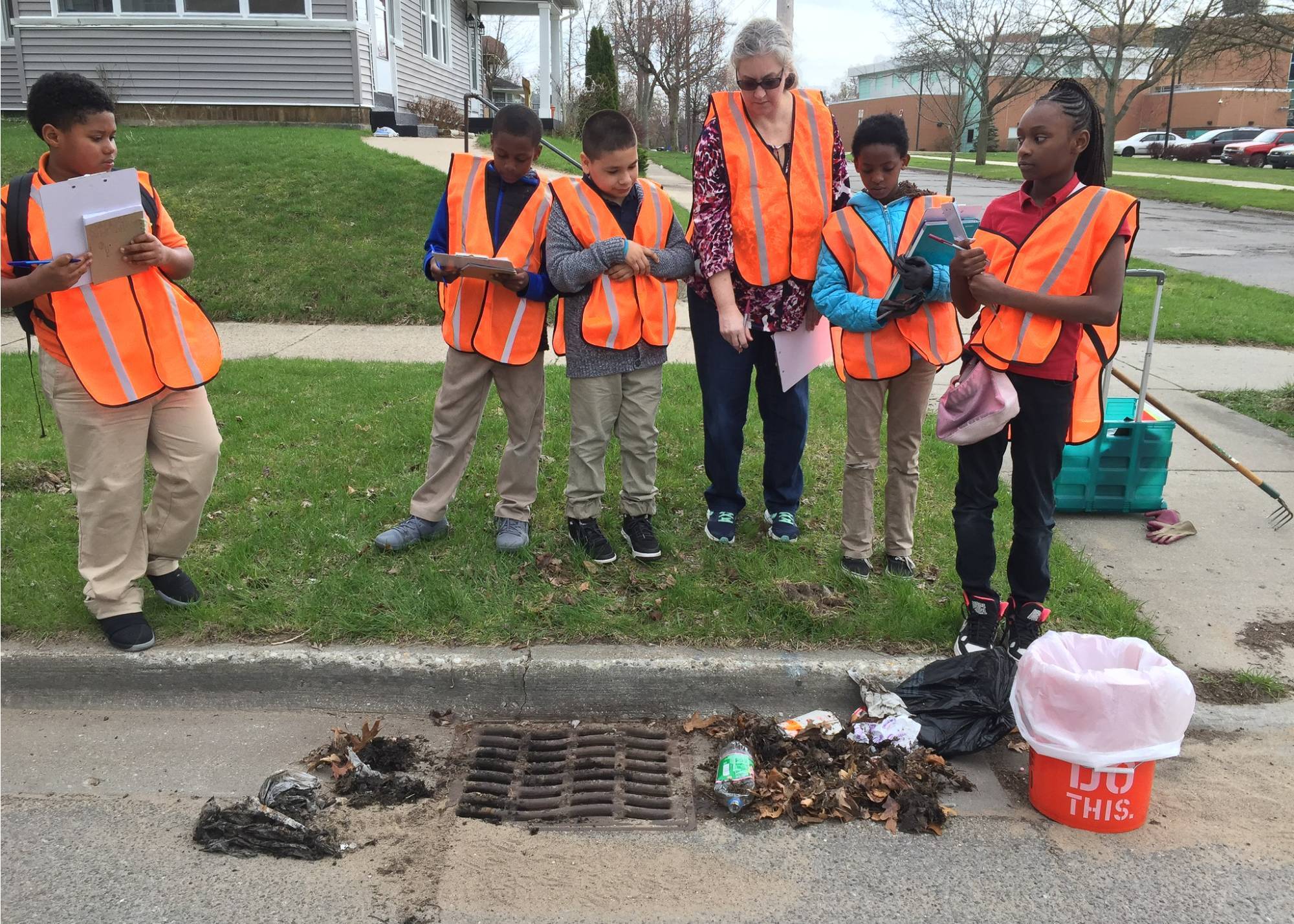 students and a teacher standing next to a clogged storm drain ready to clean it up